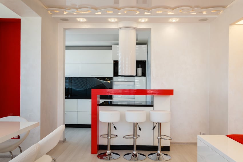Modern kitchen with red quartz countertop, bar stools, peninsula, range hood, cabinets, oven, and ceiling lights
