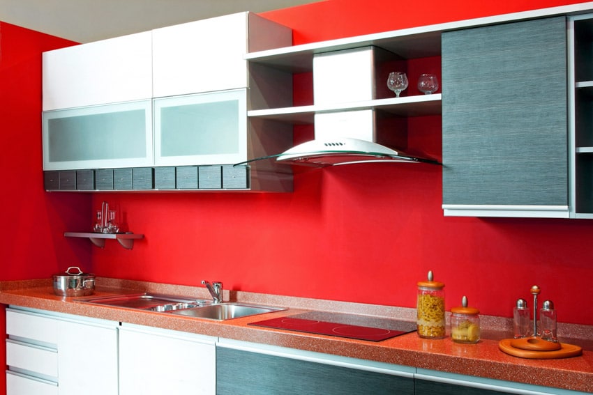 Modern kitchen with red quartz countertop, cabinets, range hood, induction stove, and red backsplash