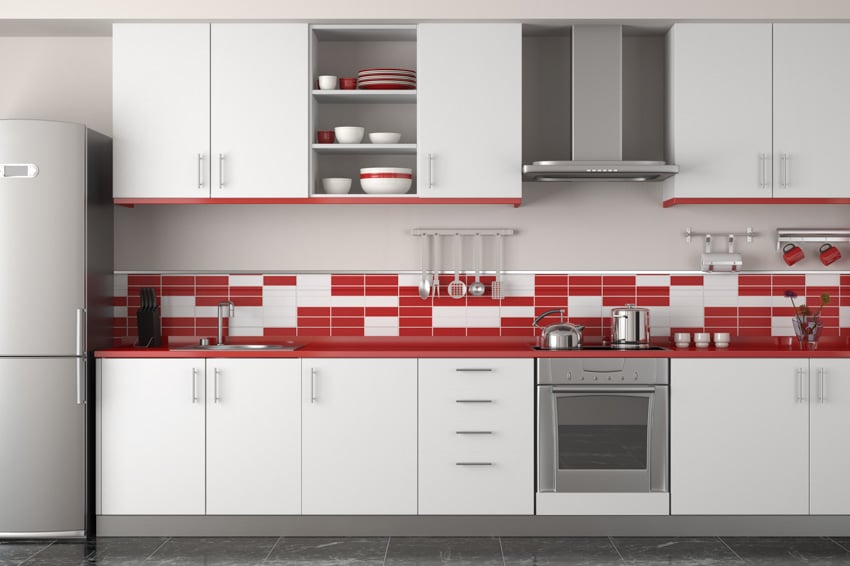 Modern kitchen with red quartz countertop, white cabinets, tile backsplash, oven, range hood, and refrigerator