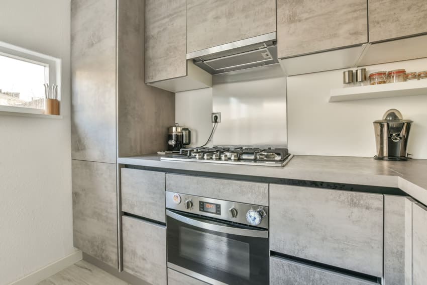 Modern rustic kitchen with oven, stove, metal backsplash, countertop, white grain cabinets, and range hood