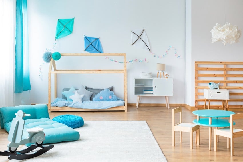 Monochromatic palette minimalist playroom features DIY aqua blue kites on empty white wall with futon and house shape bed with pillows
