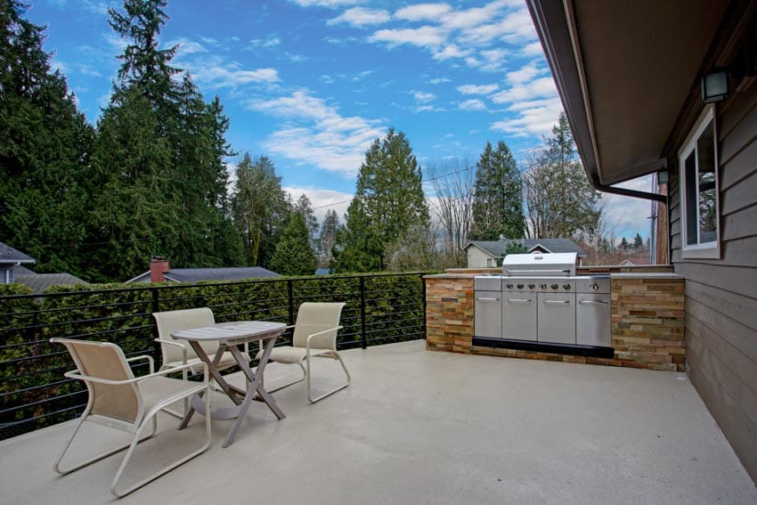 Painted concrete patio with outdoor kitchen, dining table, ledger stone countertop, grill, chairs, and table