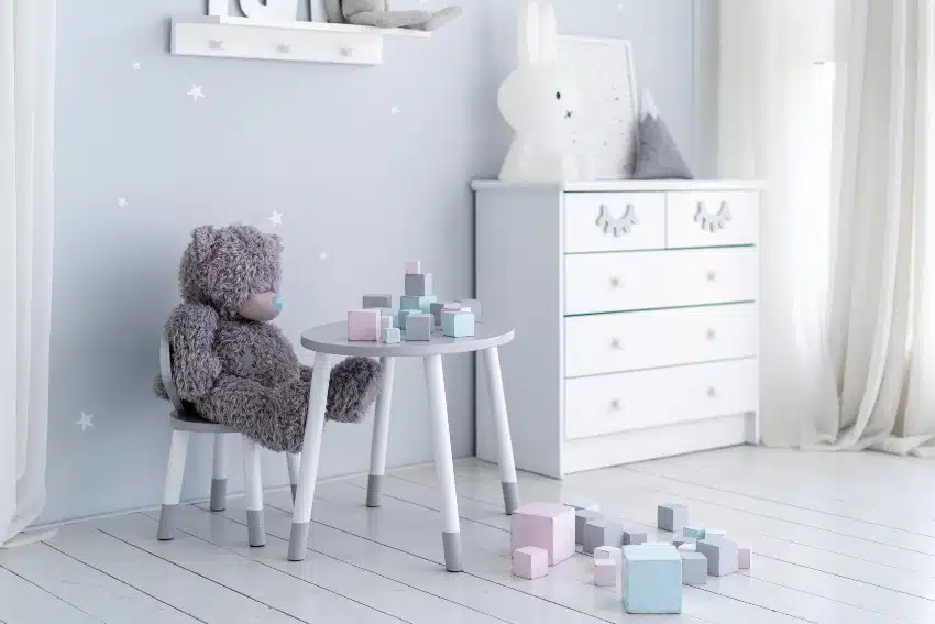 Playroom with light minimalist interior style features table and chair set, cube toys, white cabinet and a teddy bear