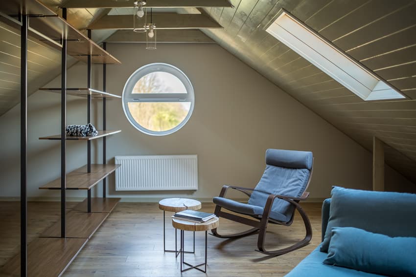 Small attic living room with shelves, rocking chair, ceiling lights, and windows
