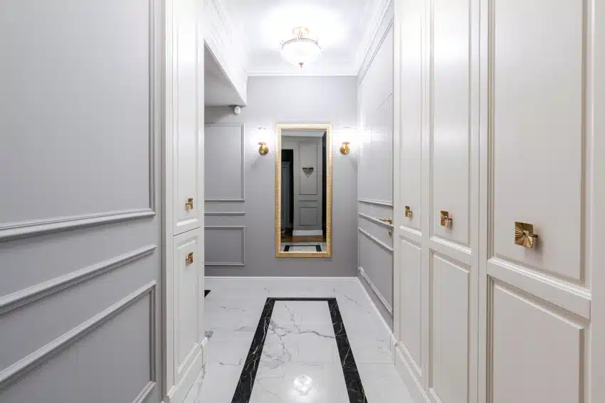 Small hallway with semi flush mount ceiling light, mirror, marble floor, and paneled walls