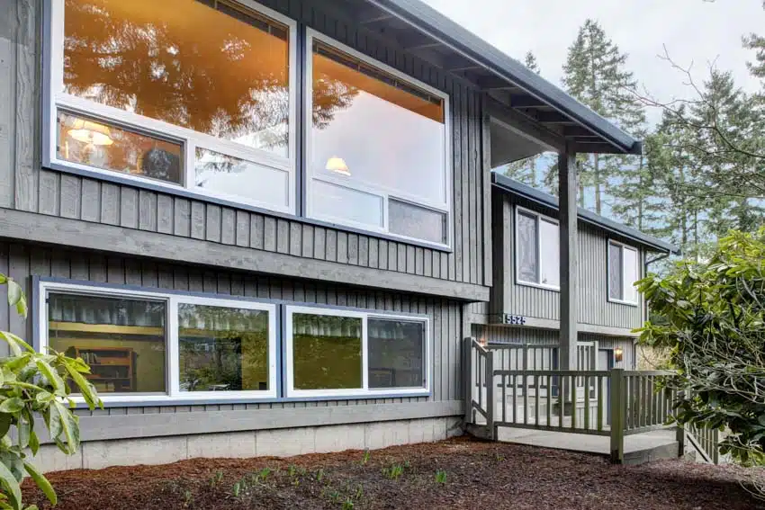 Bi level plan home with picture windows, foyer, vertical siding, and hedge plants