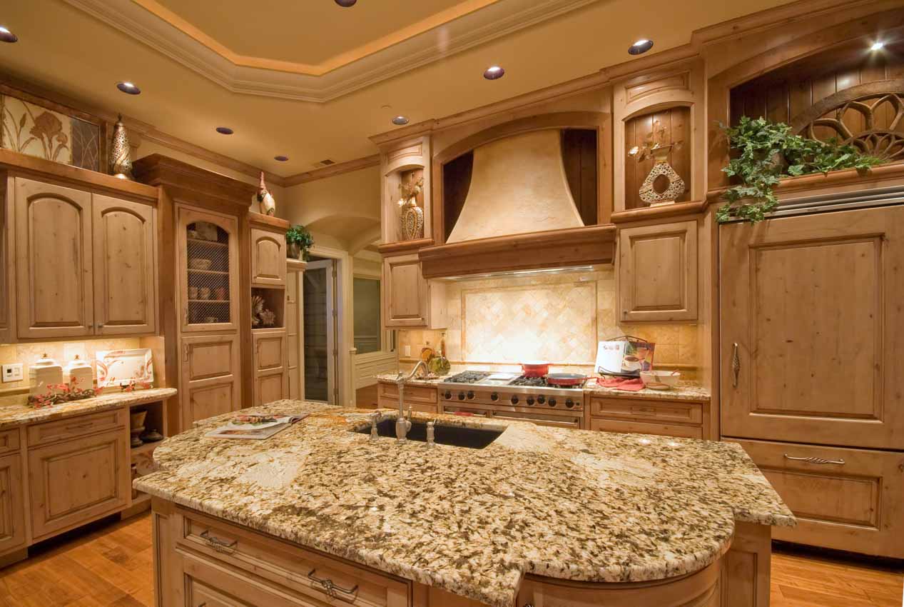 Tuscan kitchen with light wood cabinets, countertop, island, sink, faucet, and travertine tile backsplash,