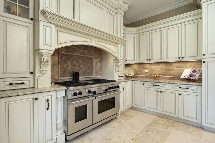 Tuscan kitchen with white washed wood cabinets, travertine backsplash, stove, oven, and tile floors