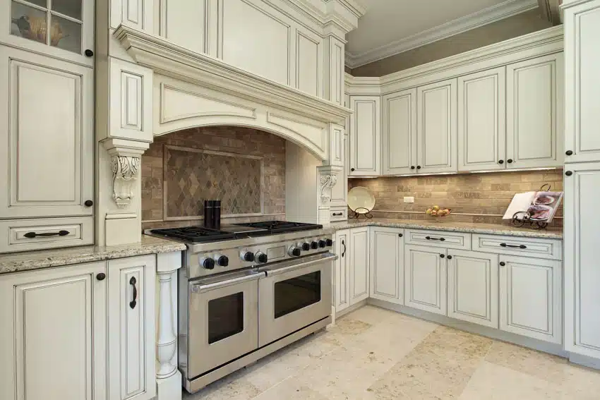 Tuscan kitchen with white washed cabinets, travertine backsplash, stove, oven, and tile floors
