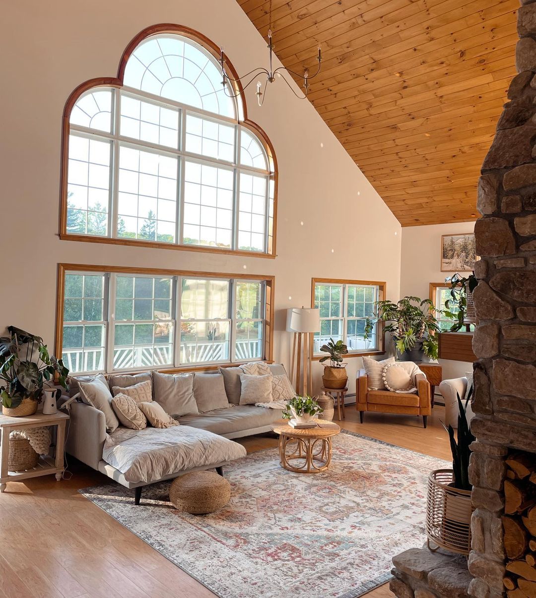 Living room with tongue and groove plank ceiling, wall of windows and stone fireplace