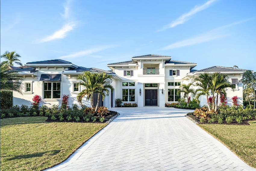 Beach house exterior with wide driveway, windows, hedge plants, front door, and lawn