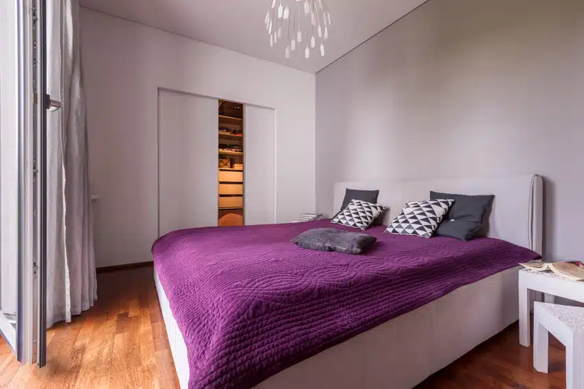 Bedroom with pillows, nightstand, closet door, and light purple gray walls