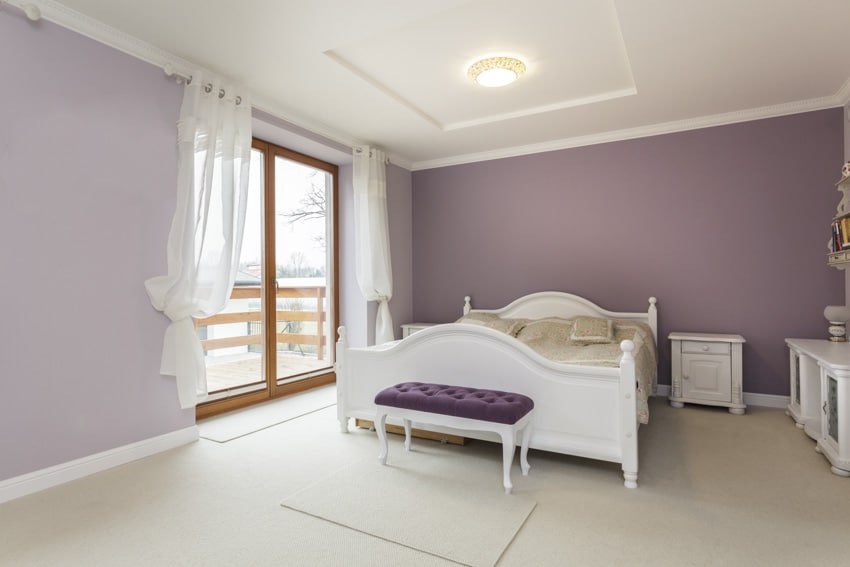 Bedroom with light purple walls, bench, glass door, nightstand, and pillows