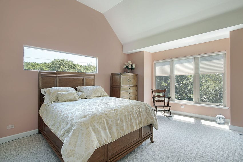 Bedroom with walnut wood bed, mattress, pillows, dresser, rocking chair, windows, and pastel pink walls