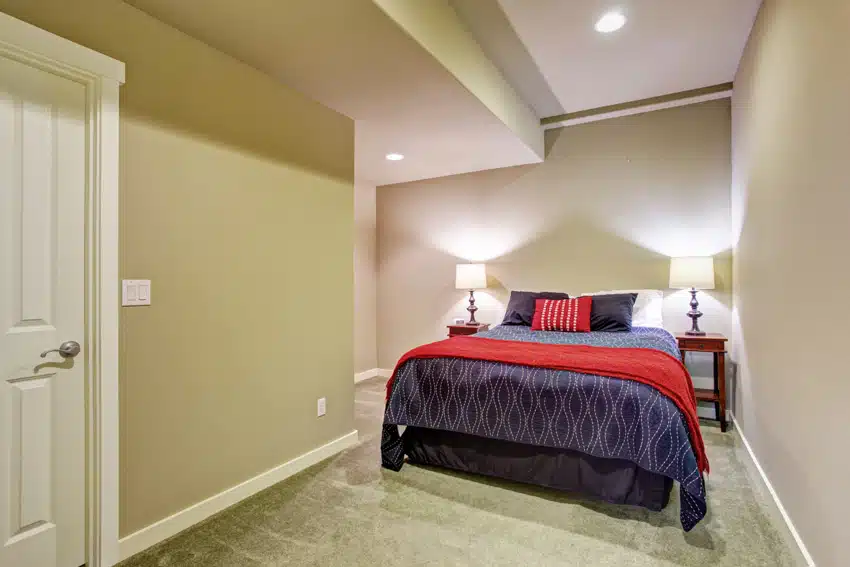 Basement bedroom with nightstands, lamps, bedding, pillows, and carpet flooring
