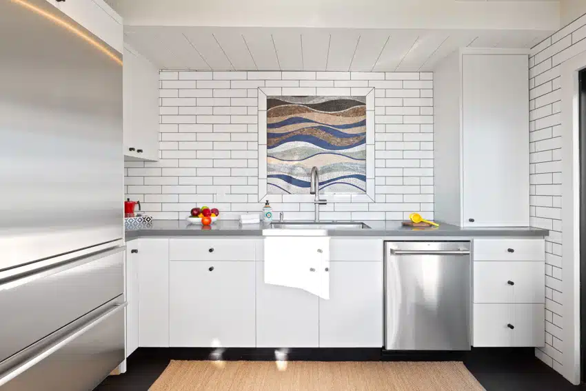 Kitchen with subway tile backsplash, countertop, dishwasher, white cabinets, and refrigerator