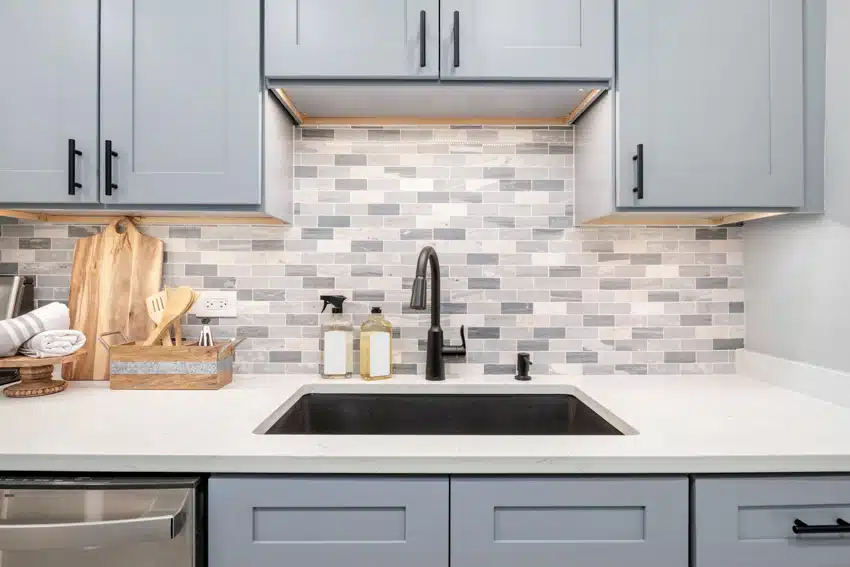 Kitchen with small subway tile backsplash, light gray cabinets, sink, and faucet