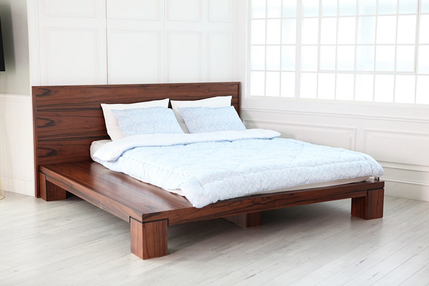 Minimalist bedroom with walnut wood bed, mattress, pillows, and glass block window