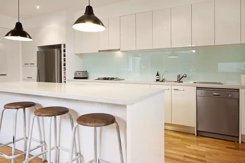 Modern kitchen with glass backsplash, island, countertops, white cabinets, bar stools, pendant lights, dishwasher, and wood floors