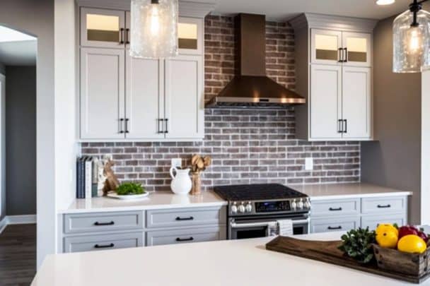 Modern Farmhouse Kitchen Backsplash Ideas Materials Options   Modern Farmhouse Kitchen With Grey Exposed Brick Backsplash Quartz Countertops White Upper Cabinets And Grey Base Cabinets A1 608x405 