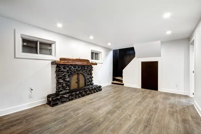 Empty basement with stone fireplace, window inserts, and wooden flooring