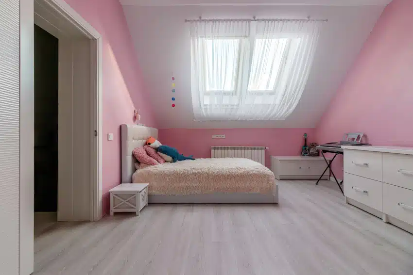 Girl's attic bedroom with pink tone, and sloping ceiling with white curtains