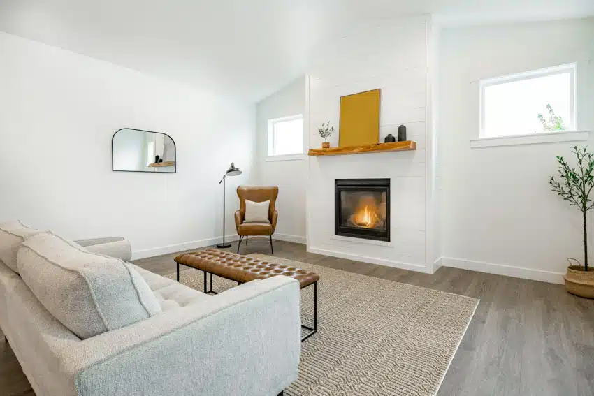 White room with electric insert, bright mantel, ottoman, loveseat, and textured carpet