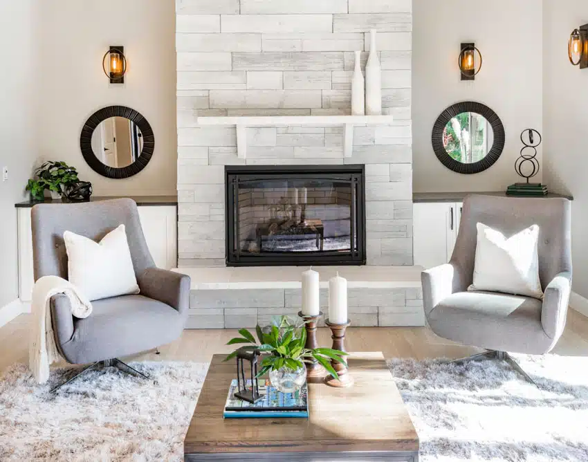 Brushed grey stone and marble fireplace, shag rug, armchairs, and rustic sconces