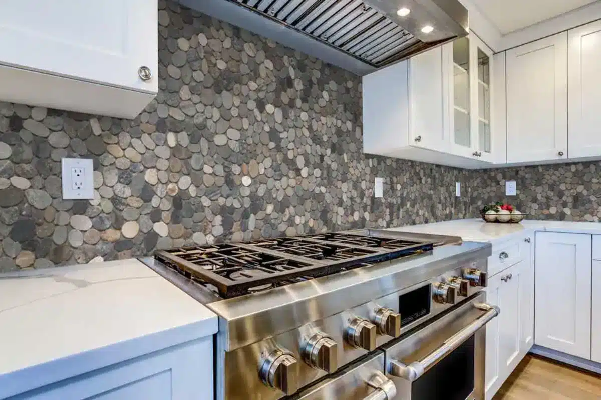 kitchen with large rock backsplash stove and cabinets