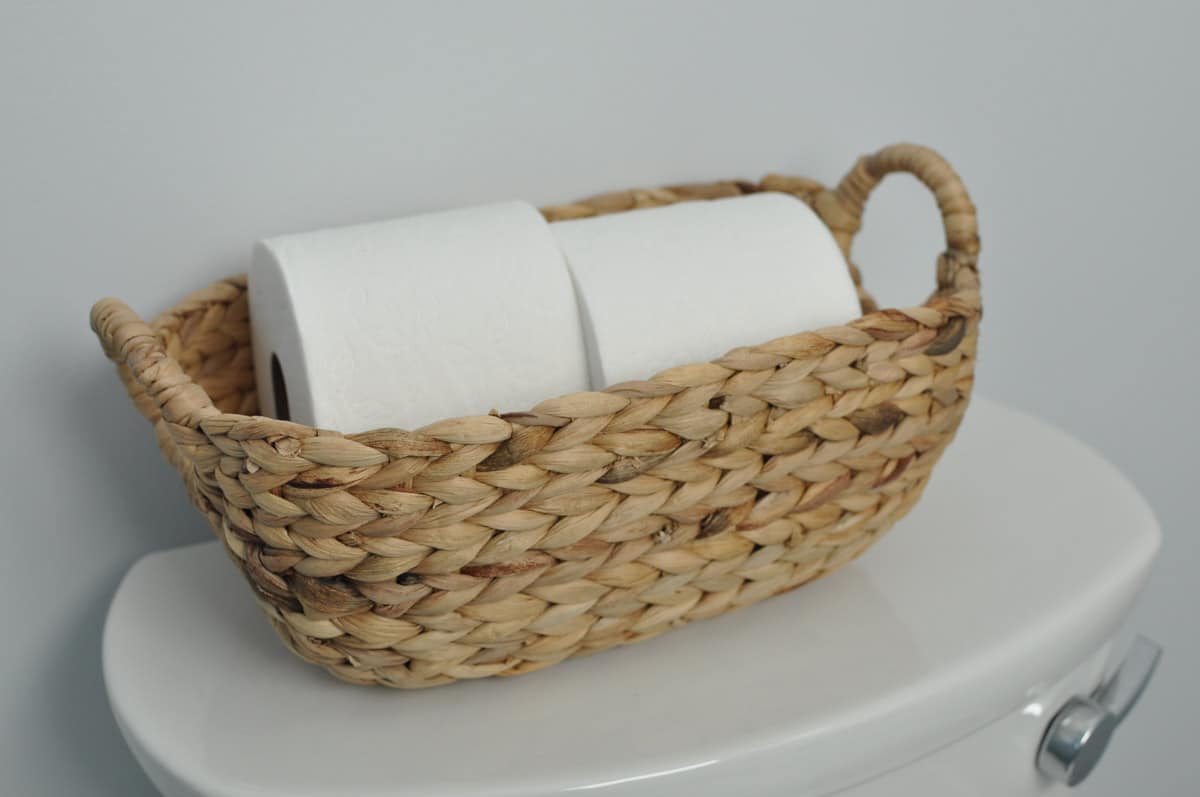 toilet with basket filled with rolls of tissue paper