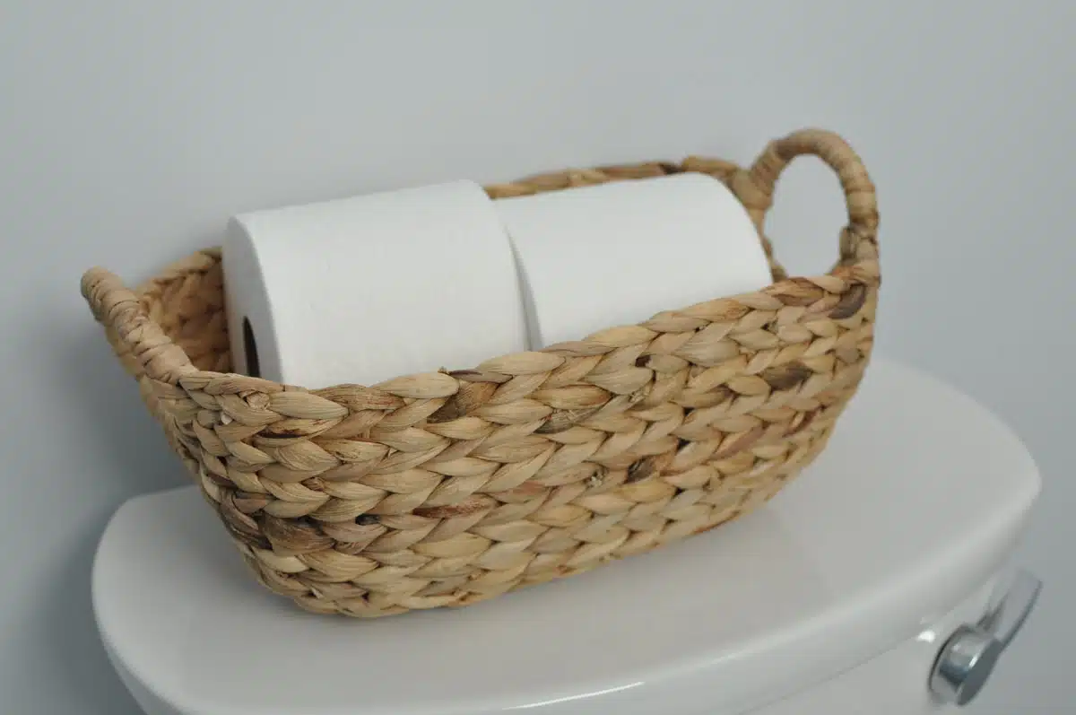 toilet with basket filled with rolls of tissue paper