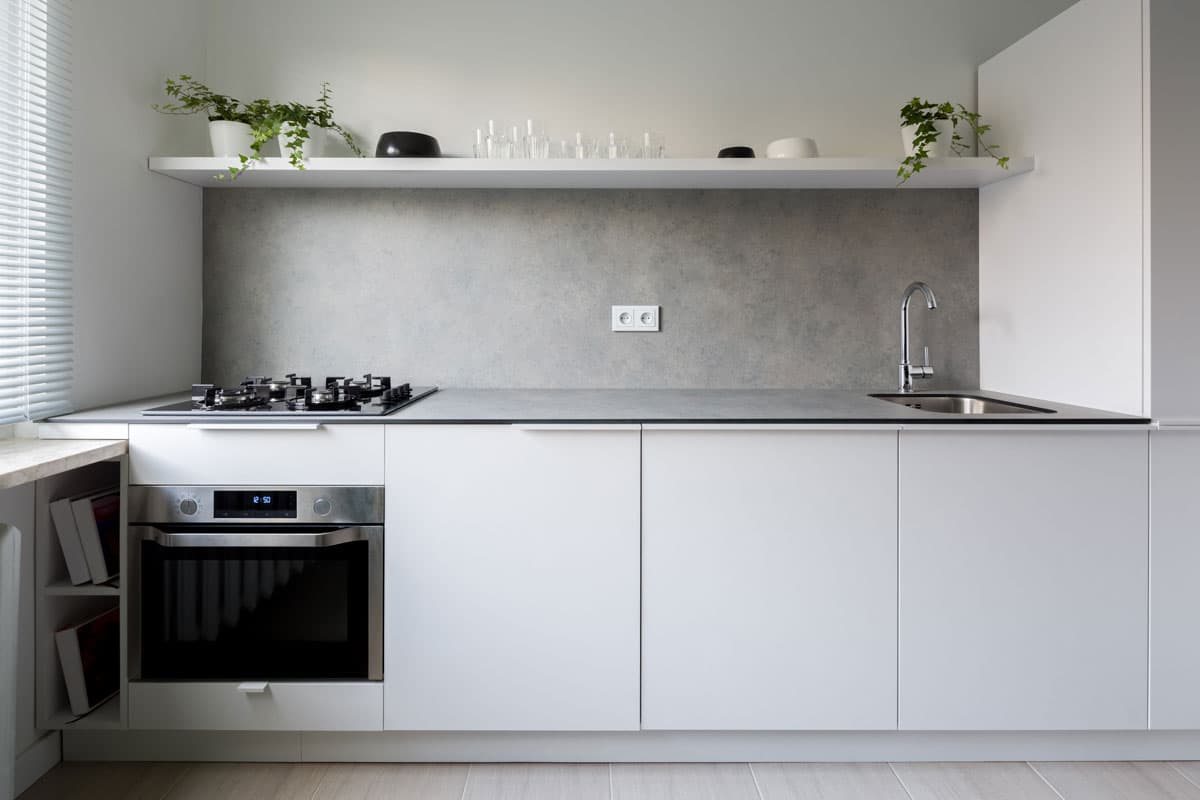minimalist kitchen with concrete backplash and white cabinets