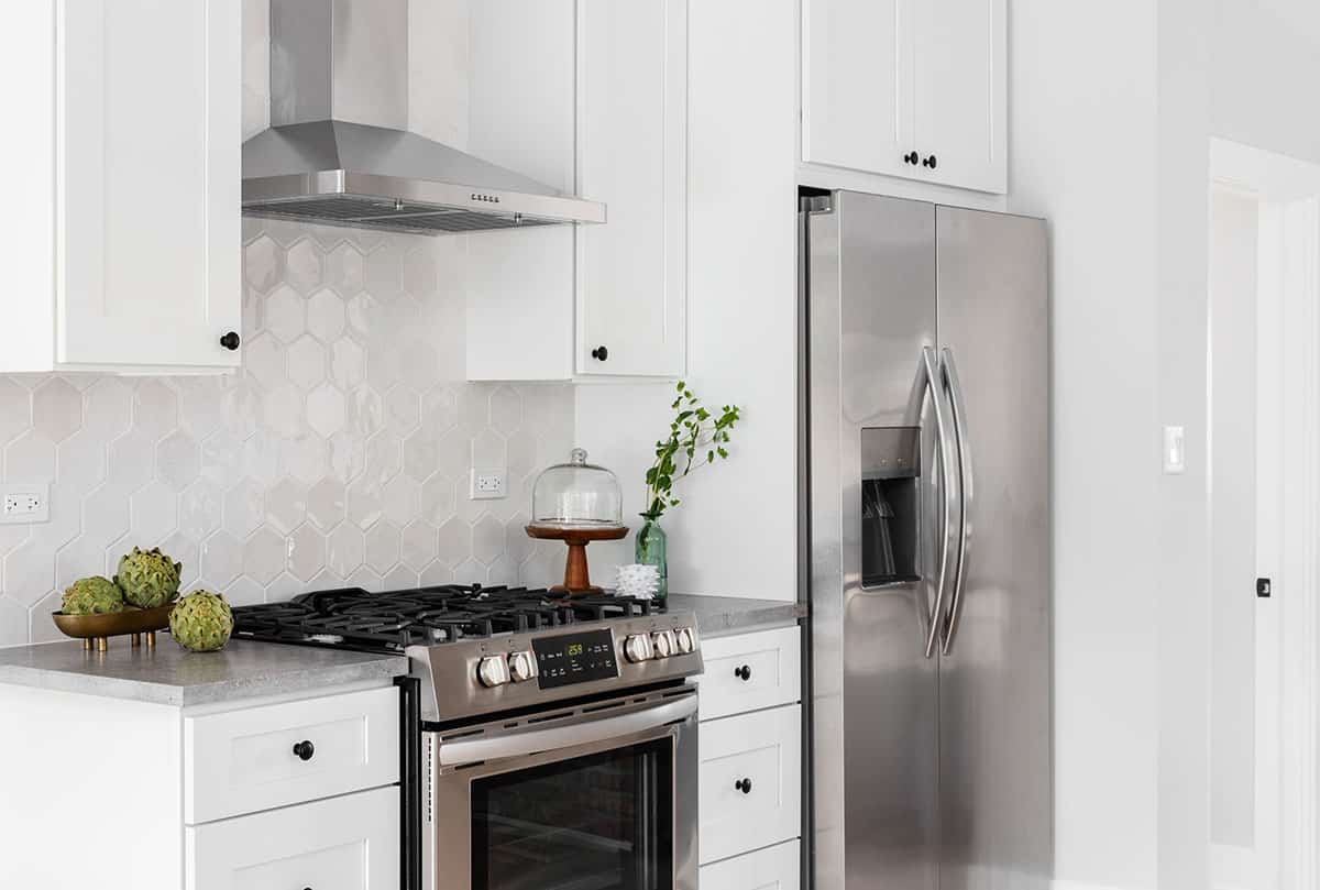 Kitchen with white cabinets hexagon backsplash range hood