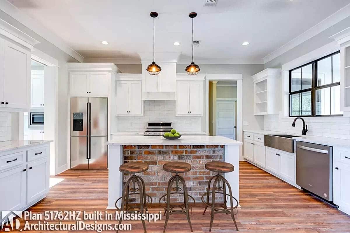 Farmhouse kitchen with brick clad island, white shaker cabinets, pendants and wood floors