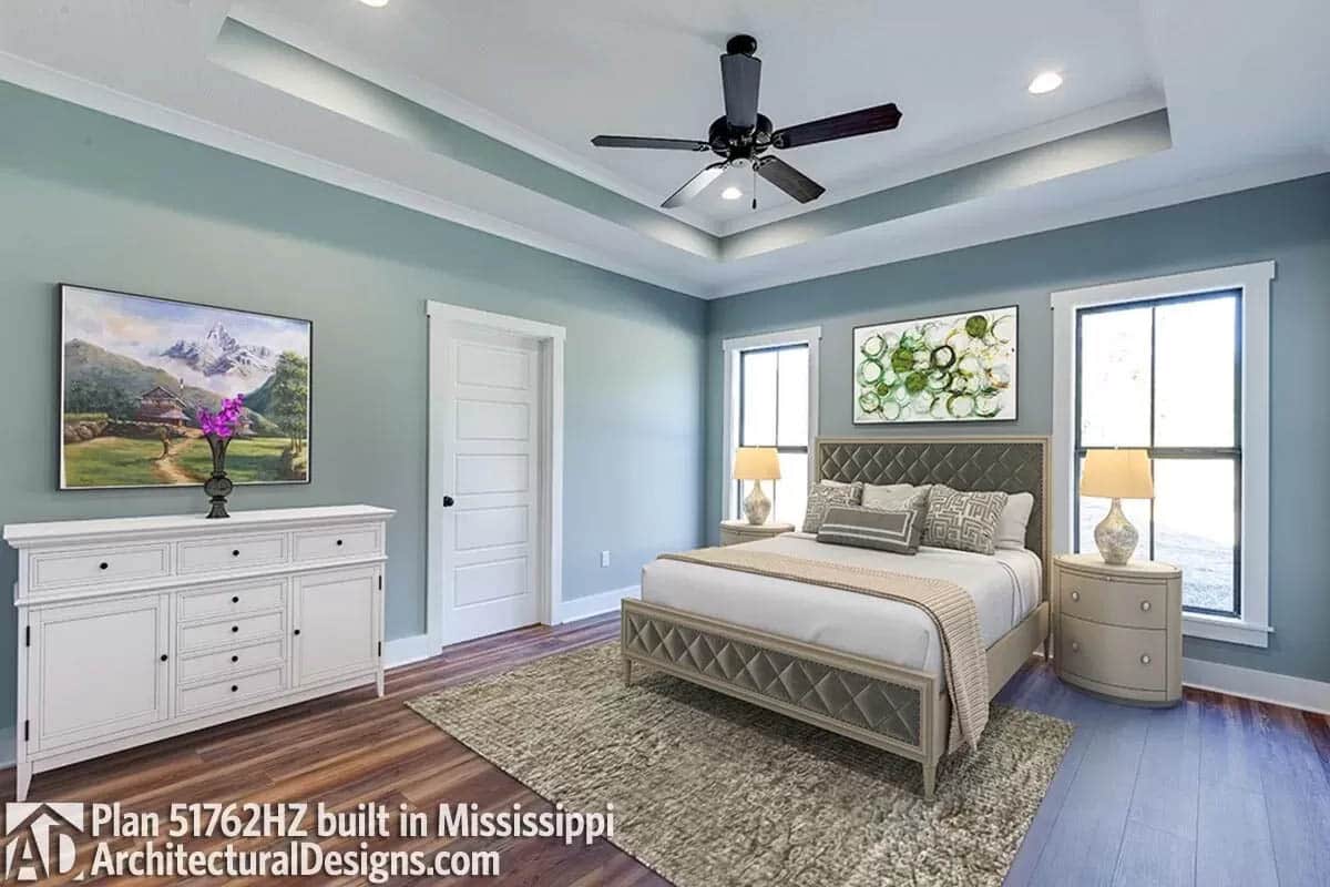 Pale blue painted master bedroom with tray ceiling ad wood plank flooring