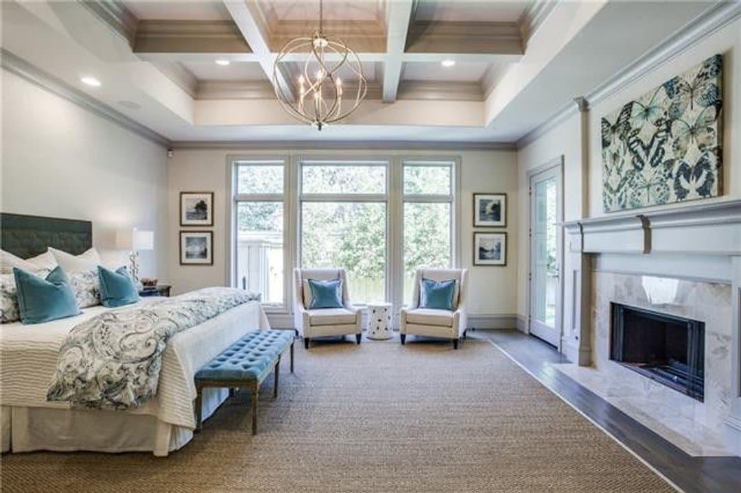 Primary bedroom with large windows, fireplace and coffered ceiling feature with globe chandelier