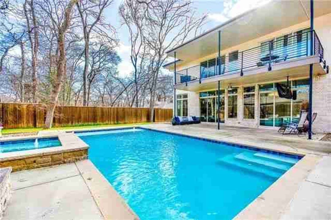 Rear of home with covered patio and upstairs balcony overlooking pool