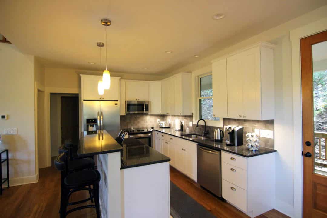 Open galley kitchen with breakfast bar and black granite counters and white cabinets