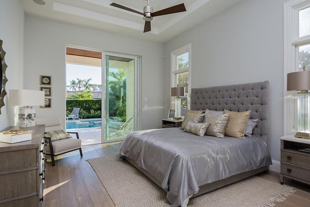 Master bedroom with grey tufted bed and doors to the swimming pool patio