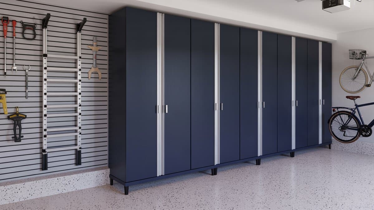 Row of tall navy blue garage cabinets with silver handles beside a gray slatwall panel holding tools and an extension ladder